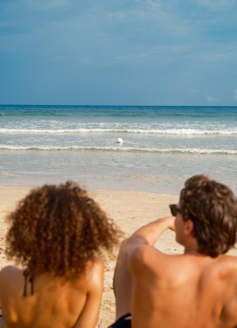 Madre e figli sorridenti camminano sulla spiaggia con il mare sullo sfondo.